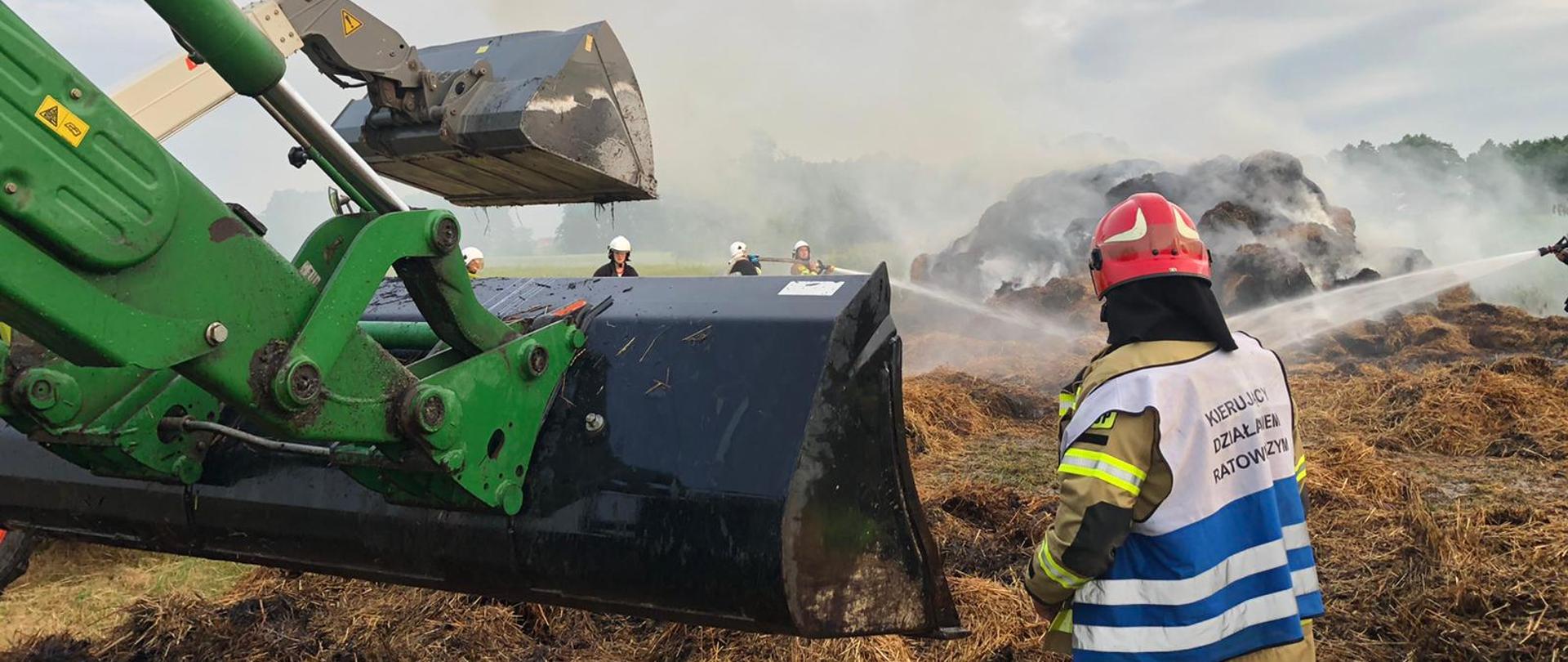Widoczne miejsce zdarzenia: płonie siano w stogu strażacy prowadzą działania gaśnicze.