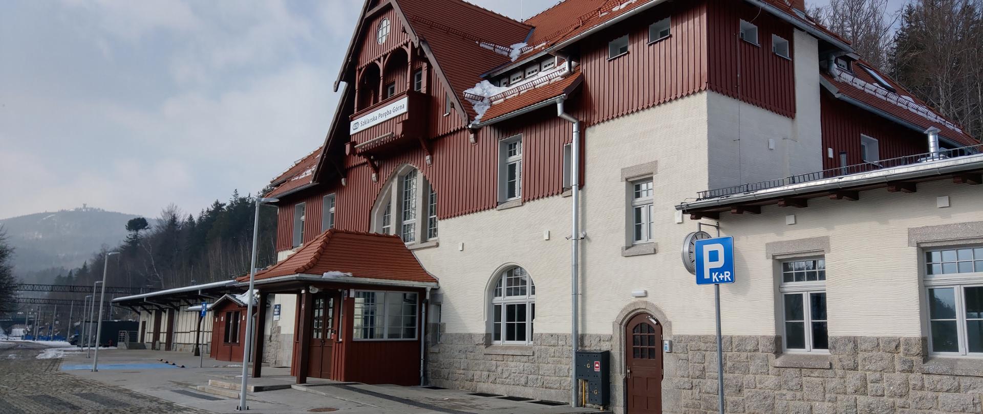 Na zdjęciu widać zmodernizowany budynek zabytkowego dworca kolejowego w Szklarskiej Porębie. Elewacja jest jasna, dach budynku w ciemnym kolorze. 