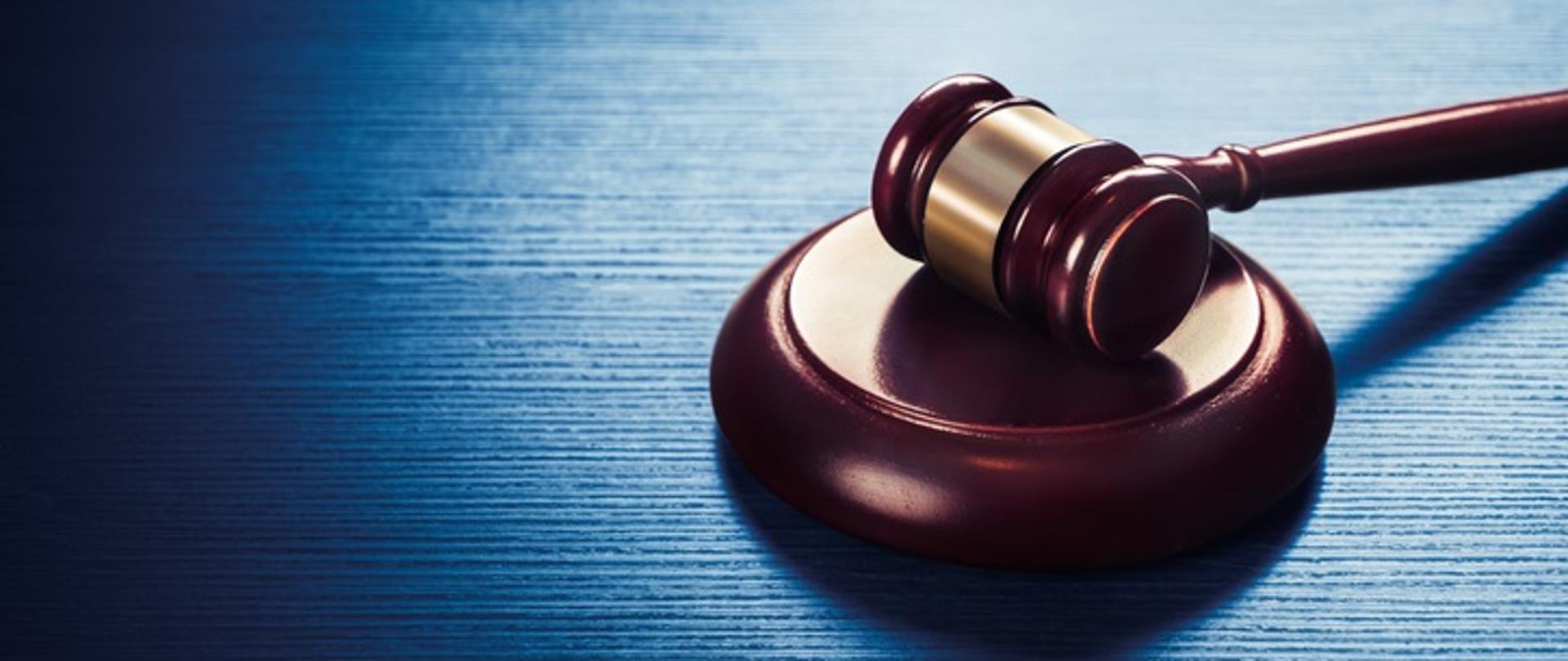 Obraz o wysokim kontraście drewnianego młotka sędziego w kolorze brązowym ze złoconym metalowym pierścieniem na niebieskim drewnianym tle.