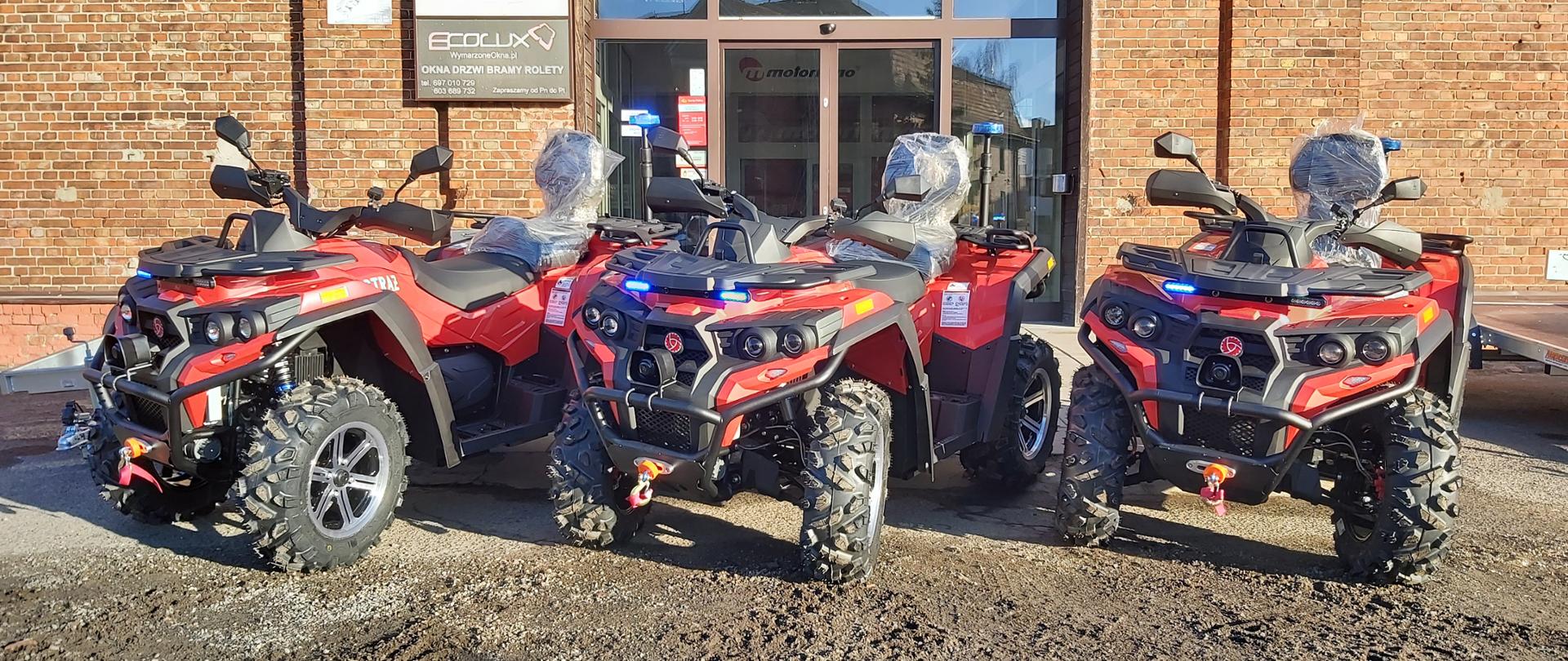 Na zdjęciu widać trzy quady w kolorze czerwonym z włączonymi sygnałami w kolorze niebieskim.