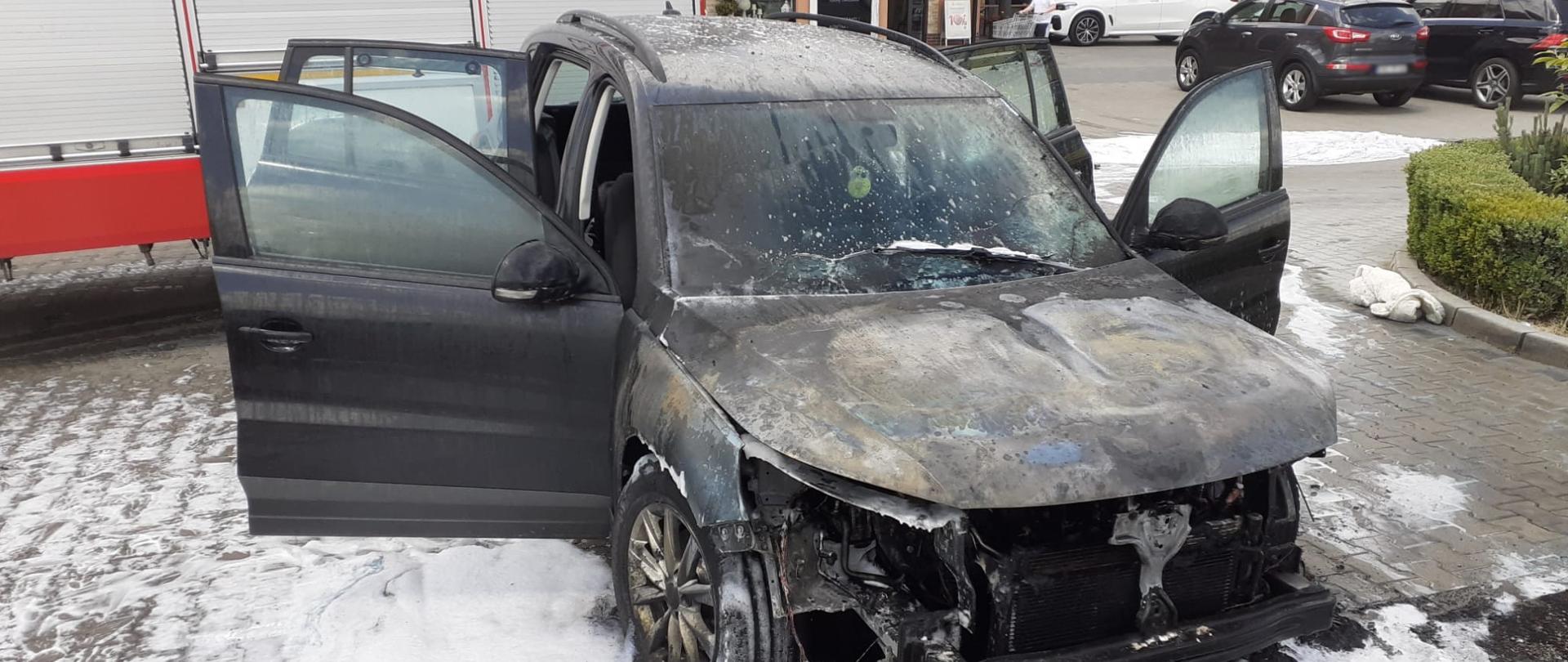 Spalony samochód osobowy a za nim samochód pożarniczy.