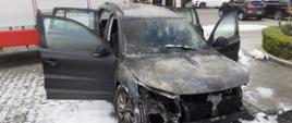 Spalony samochód osobowy a za nim samochód pożarniczy.
