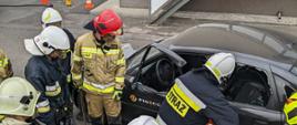 Słuchacze Szkolenia Podstawowego Strażaków Ratowników OSP podczas zajęć praktycznych z ratownictwa technicznego. Instruktor nadzoruje kursanta podczas otwarcia drzwi przy pomocy narzędzi hydraulicznych.