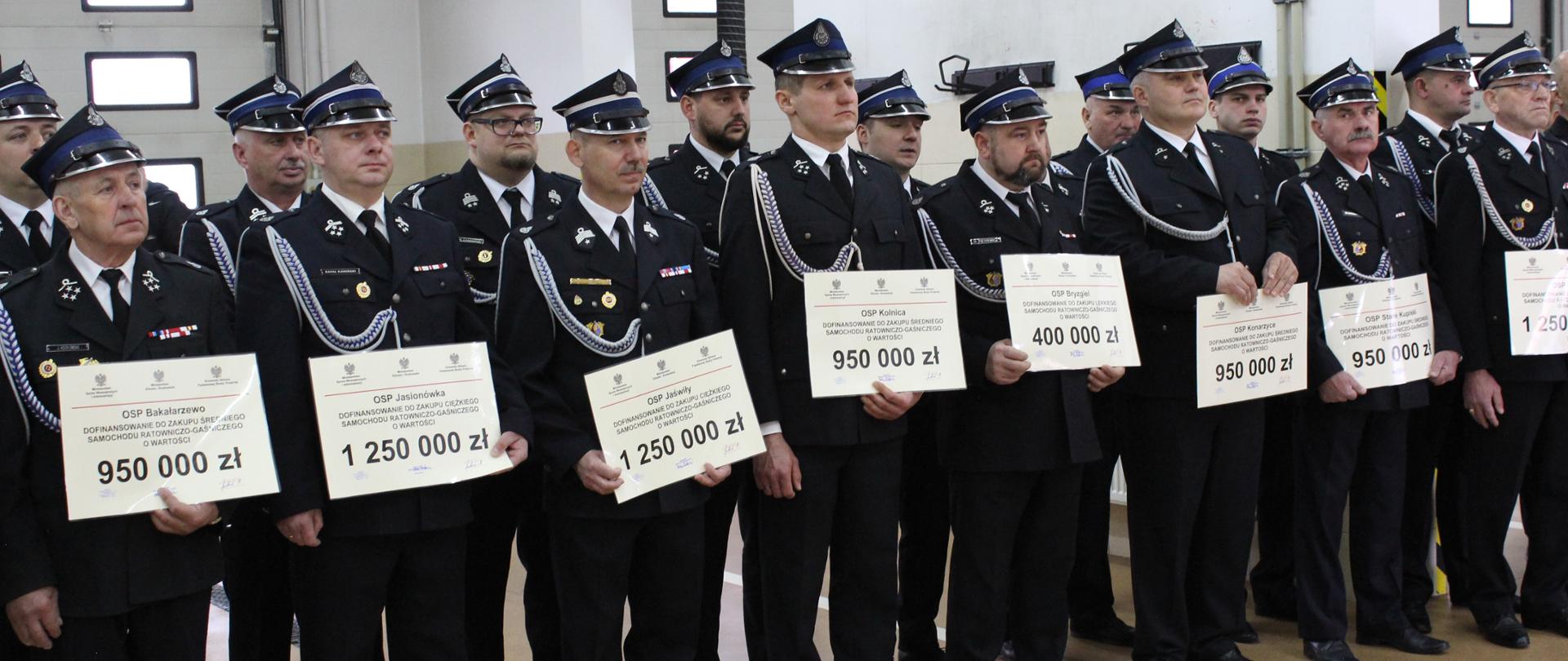 zdjęcie grupowe przedstawicieli jednostek OSP trzymający otrzymane promesy na zakup pojazdów pożarniczych 