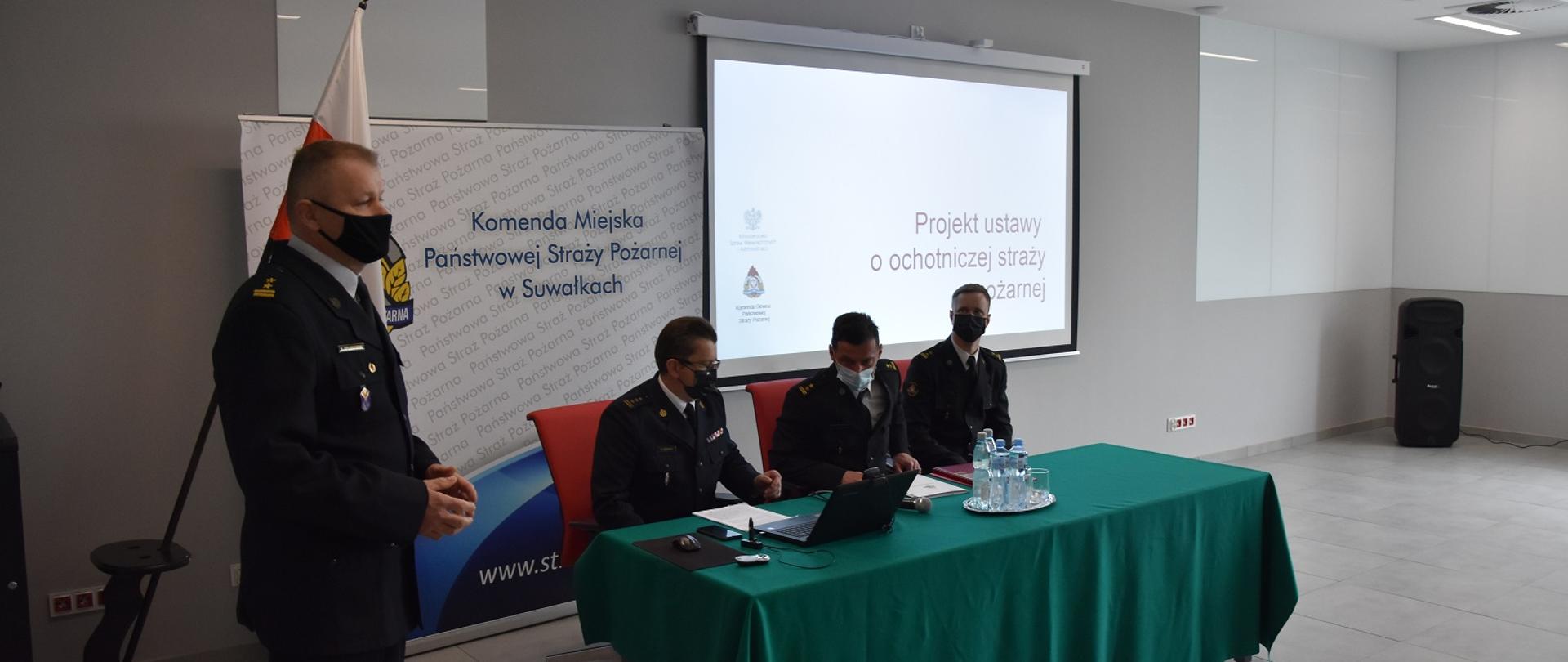 Zdjęcie obrazuje 4 strażaków w mundurach wyjściowych w tle flaga Polski 