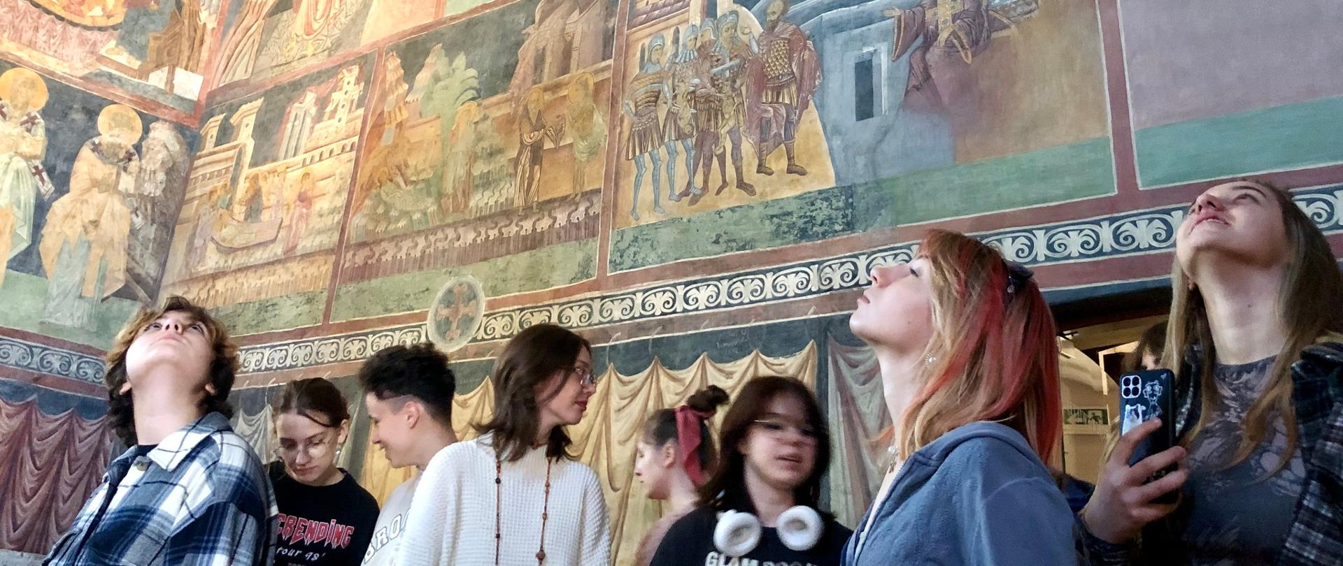 Uczniowie oglądają freski w Kaplicy Trójcy Świętej w Zamku Lubelskim w Lublinie. Niektóry z nich mają głowy zadarte do góry i uniesiony wzrok.
