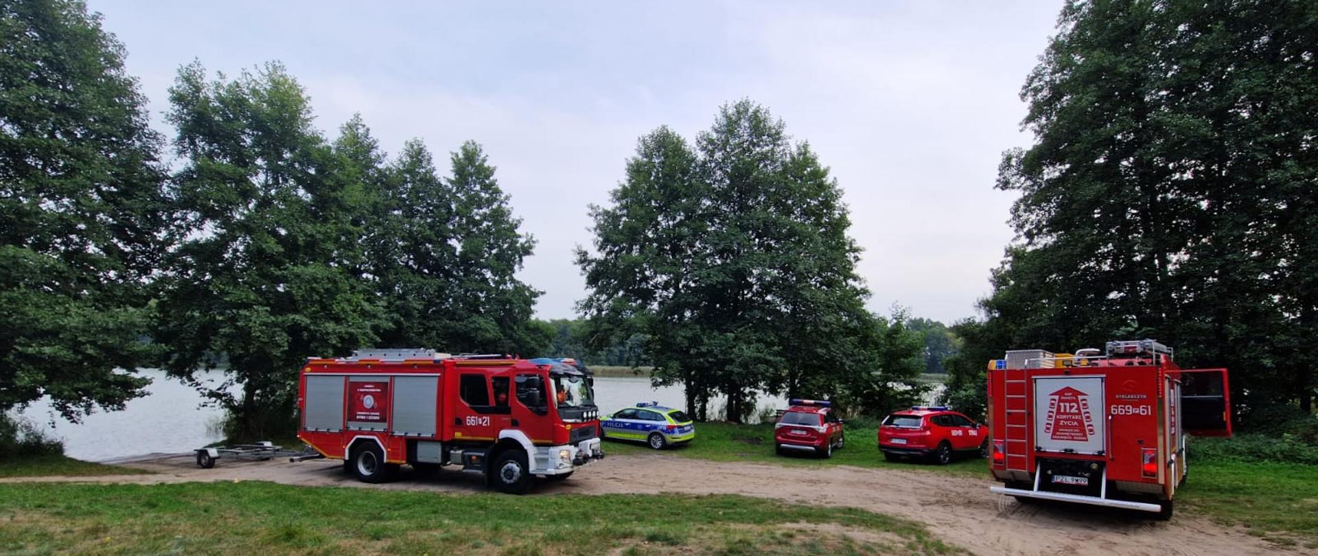 Samochód strażacki trawa, drzewa ,brzeg jeziora, strażacy przy brzegu