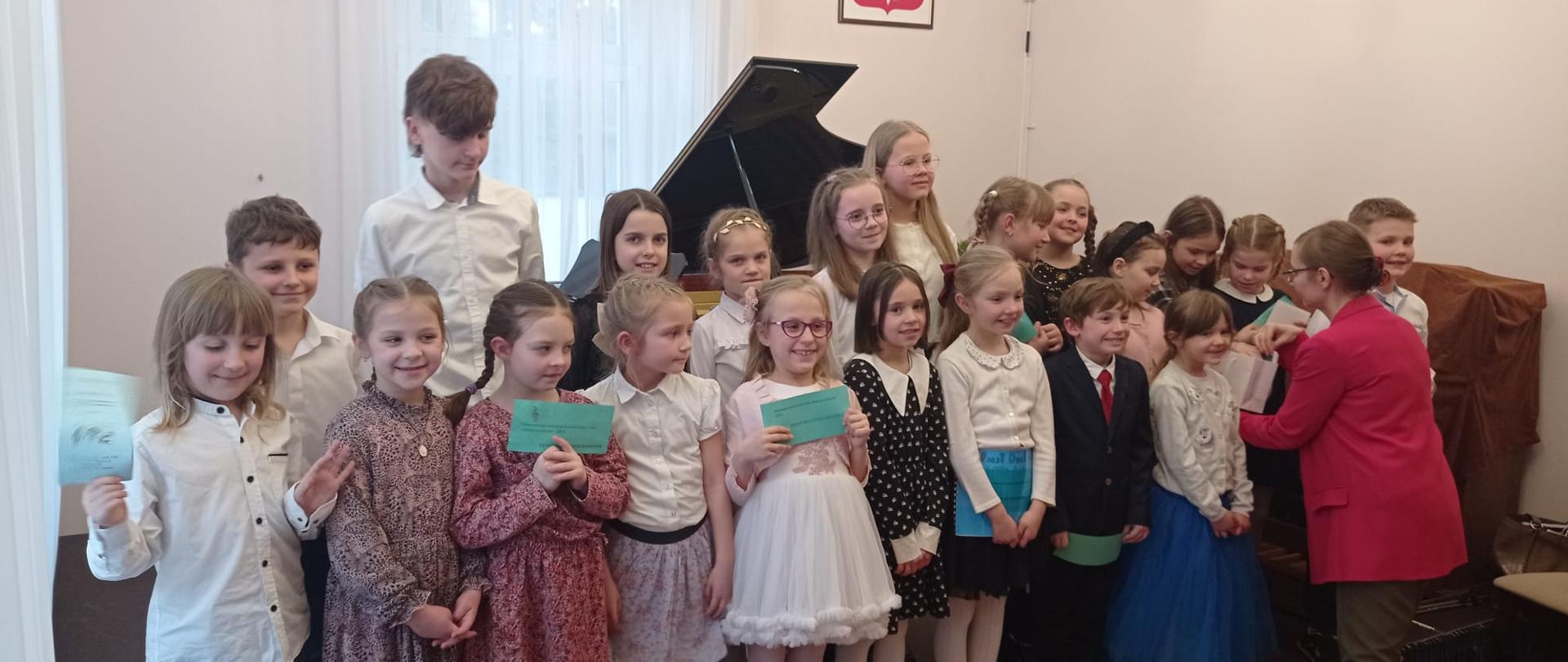Zdjęcie przedstawia uczestników międzyszkolnej prezentacji najmłodszych pianistów.