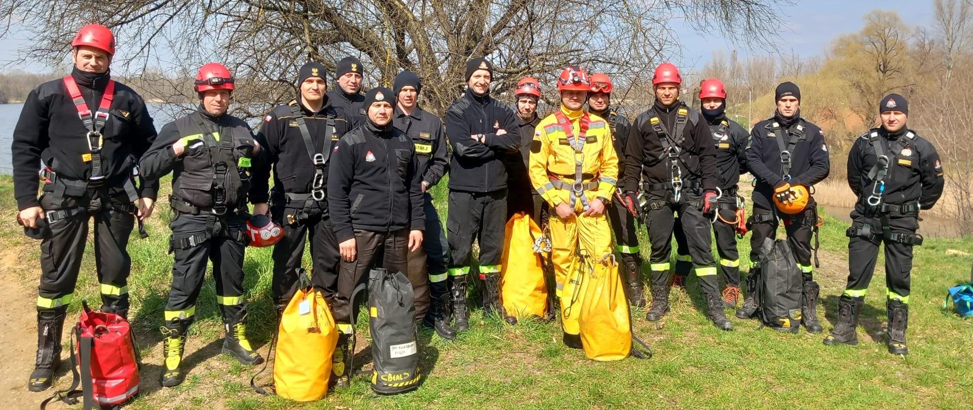 Wspólne zdjęcie grupowe instruktorów ratownictwa wysokościowego z komend powiatowych i miejskiej PSP województwa opolskiego.
Strażacy w uprzężach, ubraniach koszarowych (jeden strażak w żółtym kombinezonie). Część funkcjonariuszy posiada kaski na głowie, pozostali czapki zimowe.
