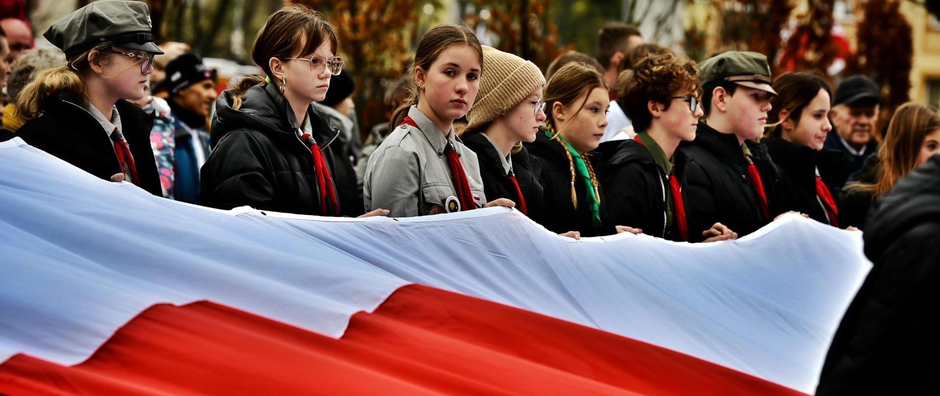 Zdjęcie przedstawia mieszkańców Gołdapi oraz przedstawicieli władz samorządowych i innych służb, którzy o godz. 12:00 na Placu Zwycięstwa w Gołdapi (nieopodal Pomnika Niepodległości) zaśpiewali hymn państwowy. Uczestnicy uroczystości trzymają flagę Rzeczypospolitej Polskiej
