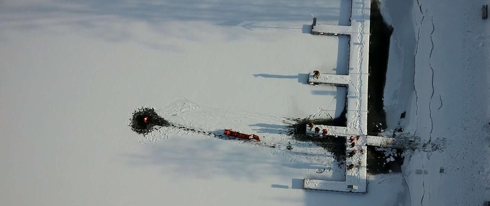 zdjęcie przedstawia zamarznięty zbiornik wodny i strażaków będących na pokrywie lodowej 