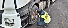 Inspektor sprawdza stan ogumienia i elementów mocujących koło pojazdu ciężarowego podczas kontroli drogowej.