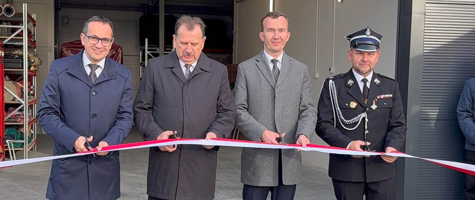 Kilku mężczyzn przecina biało-czerwoną wstęgę stojąc przed budynkiem 