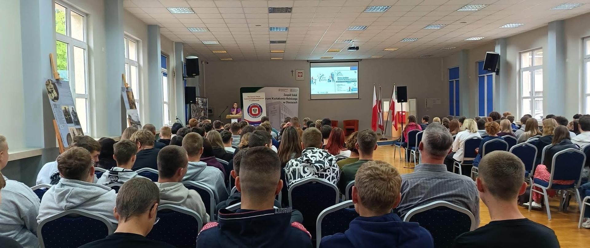 Aula z uczniami i prelegent na scenie