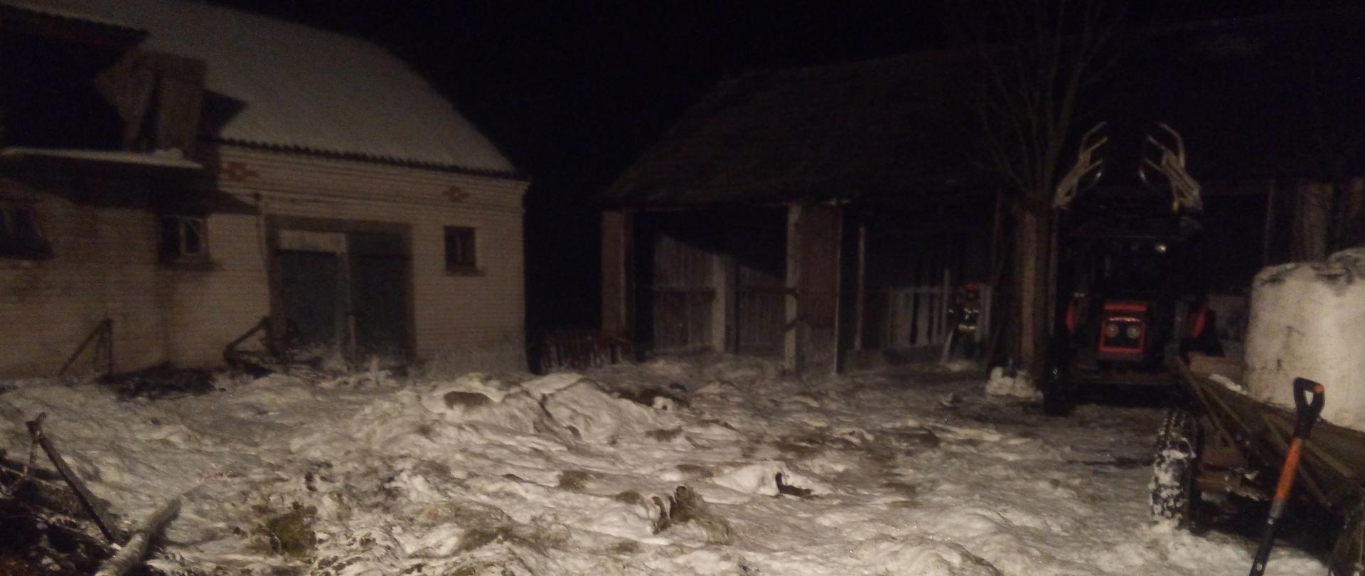 Rozrzucone na ziemi siano pokryte pianą gaśniczą na tle zabudowań gospodarczych.