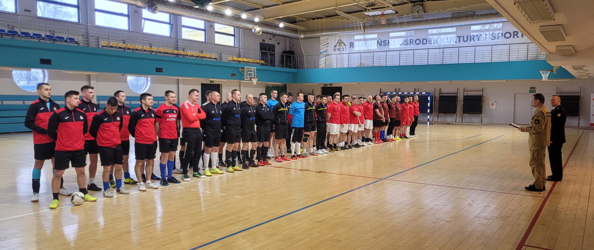 Zdjęcia przedstawiają zmagania strażaków podczas zawodów w piłce nożnej halowej. Na zdjęciach widać rozpoczęcie zawodów podczas których reprezentacje stoją w szeregu, następnie widoczne są rozgrywki. Zawodnicy ubrani są w stroje sportowe. Na koniec wykonano zdjęcie grupowe wszystkich uczestników.