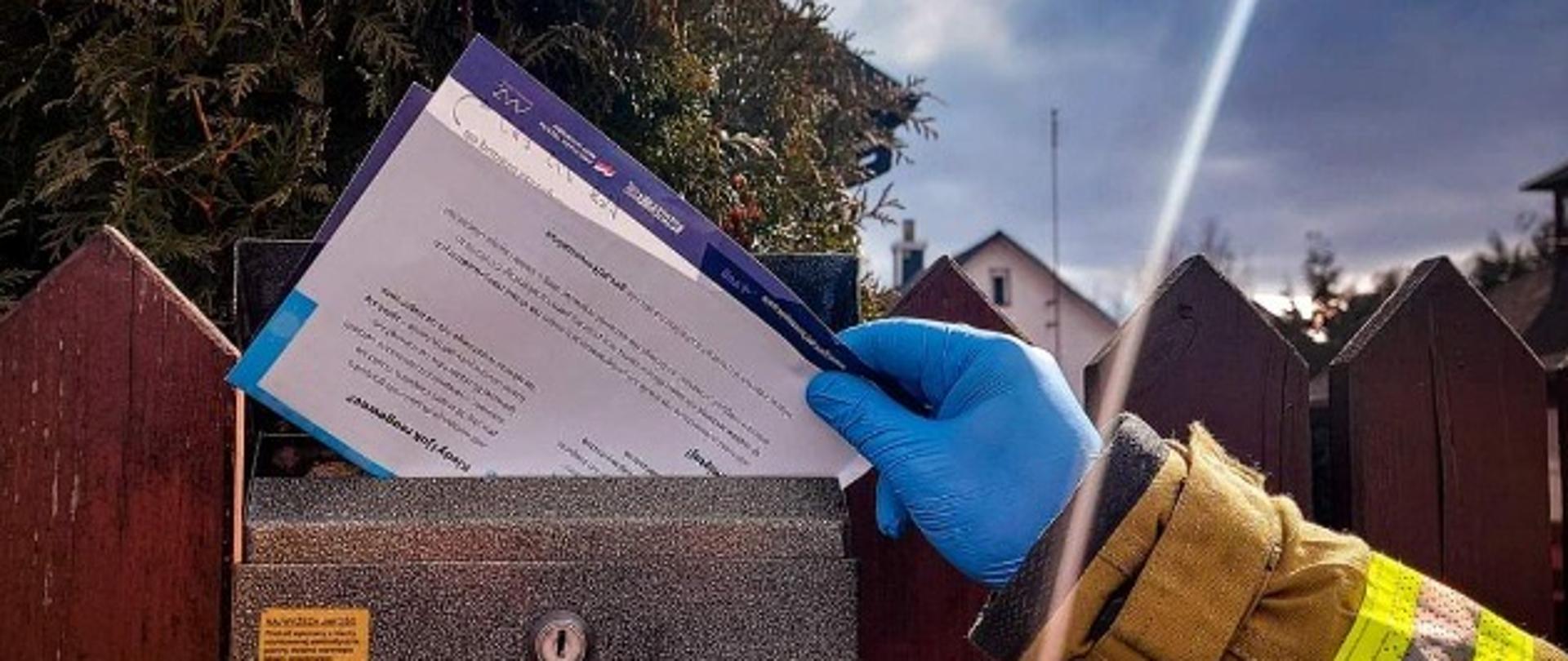 Ulotka informacyjna wkładana jest przez strażaka do skrzynki pocztowej. 