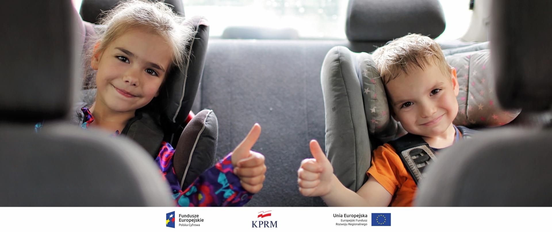 Dwoje dzieci siedzących w fotelikach, na tylnym siedzeniu auta. Oboje wykonują gest - trzymają kciuki w górę.