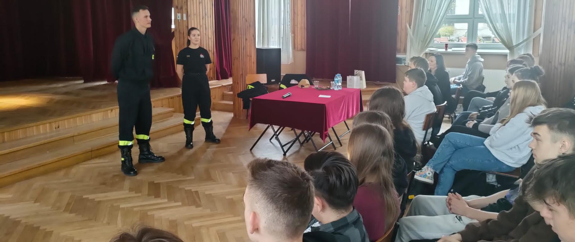 Kadet wraz z kadetką Centralnej Szkoły PSP przemawiają do siedzących przed nimi w auli uczniów