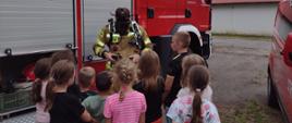 Dzieci zgromadzone przed samochodem gaśniczym, przed nimi strażak ubrany w aparat powietrzny