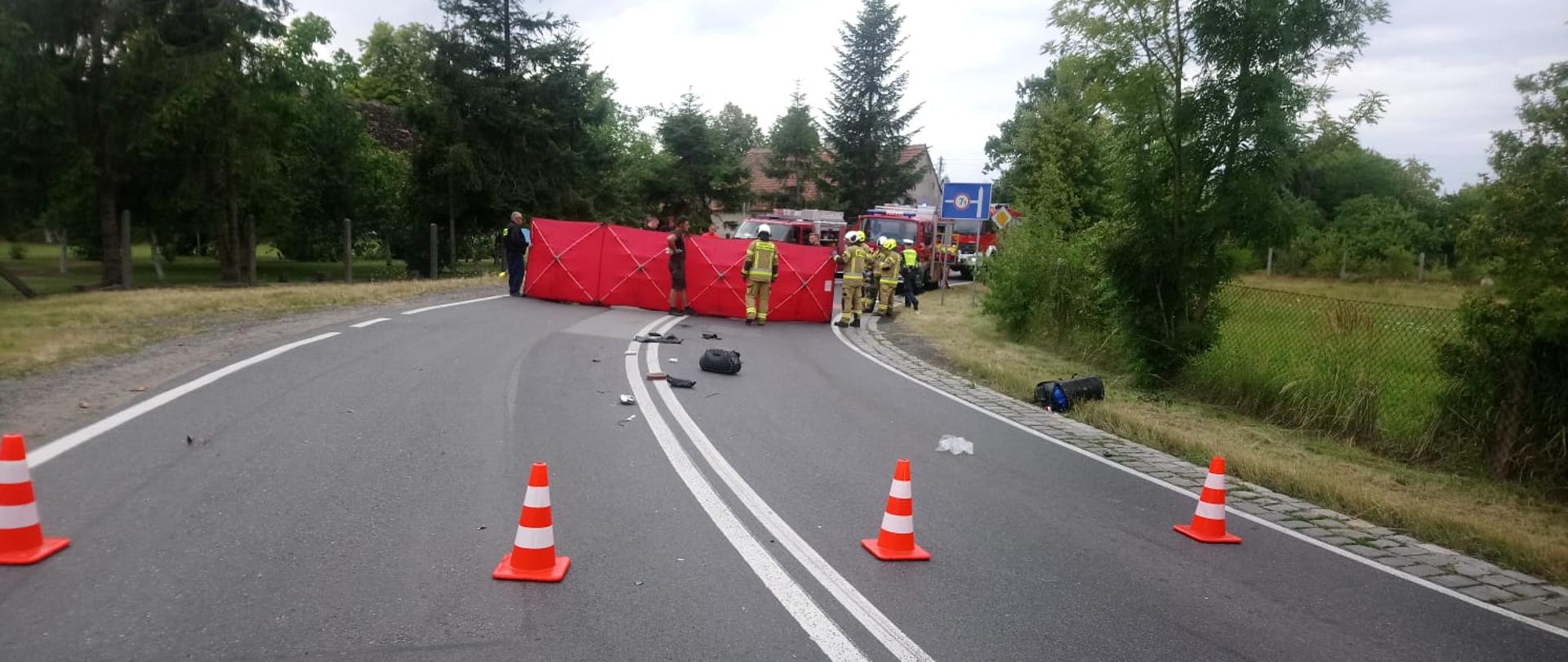 Wypadek z udziałem motocykla na drodze krajowej nr. 39 w pobliżu Rogalic - zdjęcie przedstawia jezdnię na której rozłożony jest czerwony parawan, w tle stoją strażacy oraz samochody ratownicze