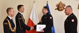 Zdjęcie przedstawia Zastępce Łódzkiego Komendanta Wojewódzkiego w Łodzi st. bryg. Sebastiana Kościstego wręczającego mł. bryg Łukaszowi Łukasikowi decyzję personalną dot. powierzenia obowiązków P.O. Zastępcy Komendanta Powiatowego PSP w Zgierzu. 