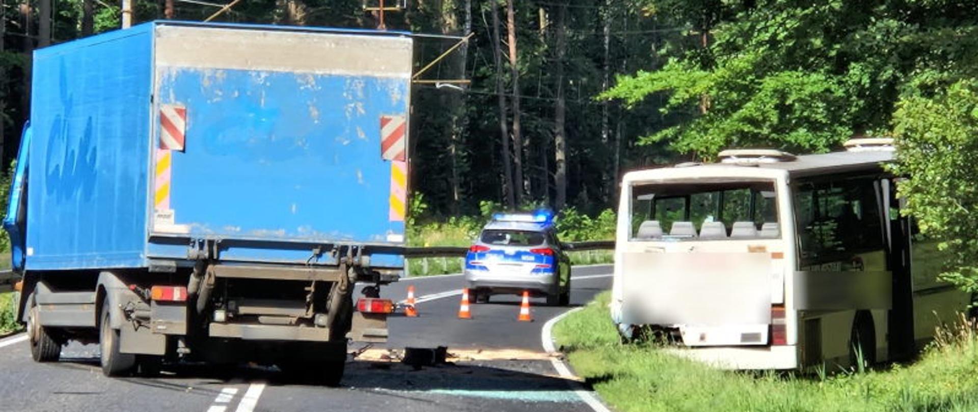 Na jezdni stoi niebieski samochód ciężarowy, w rowie stoi autobus, w oddali radiowóz policji.