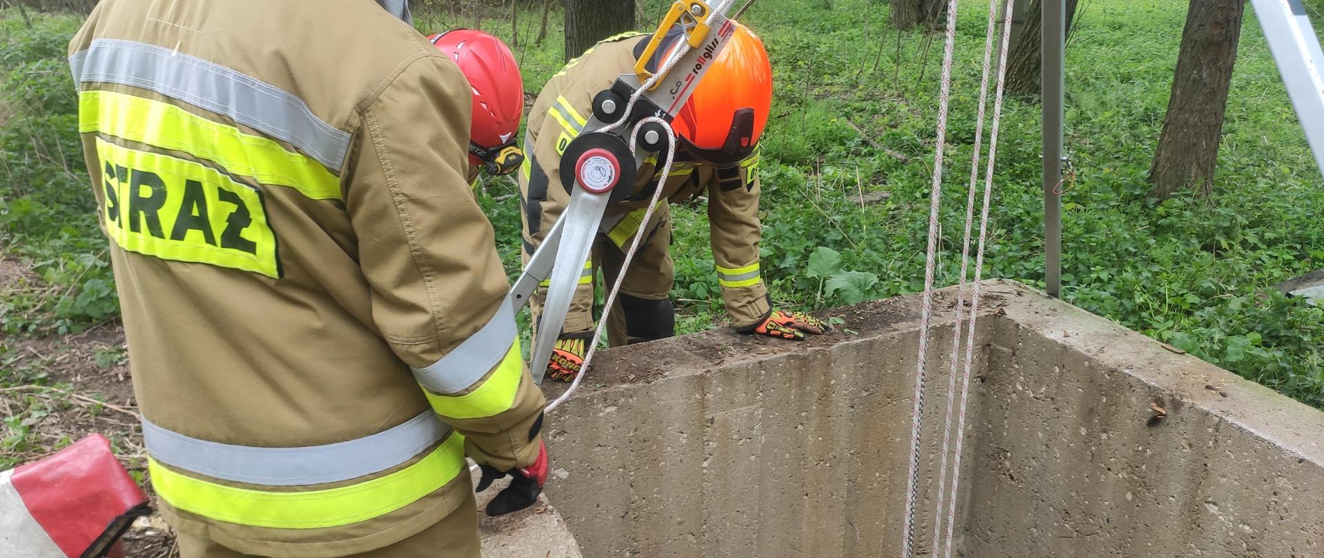 Strażacy pochyleni nad studnią z rozstawionym sprzętem wysokościowym