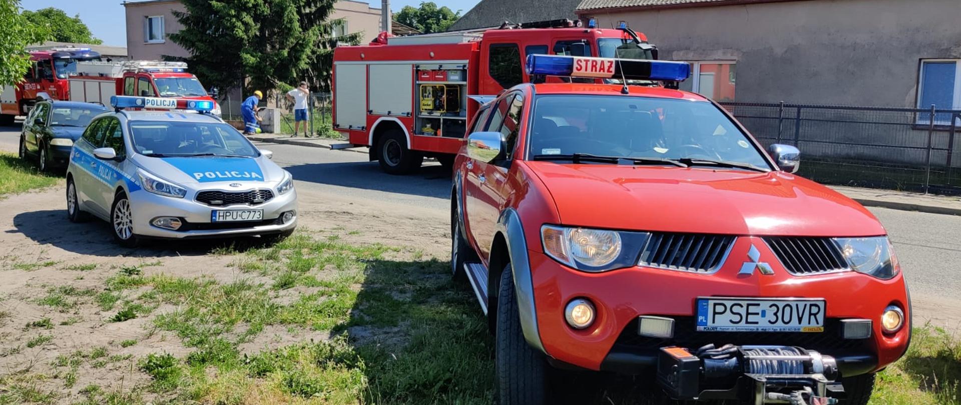 Na zdjęciu samochody ratowniczo - gaśnicze, operacyjny oraz pojazd policji w oddali mieszkańcy