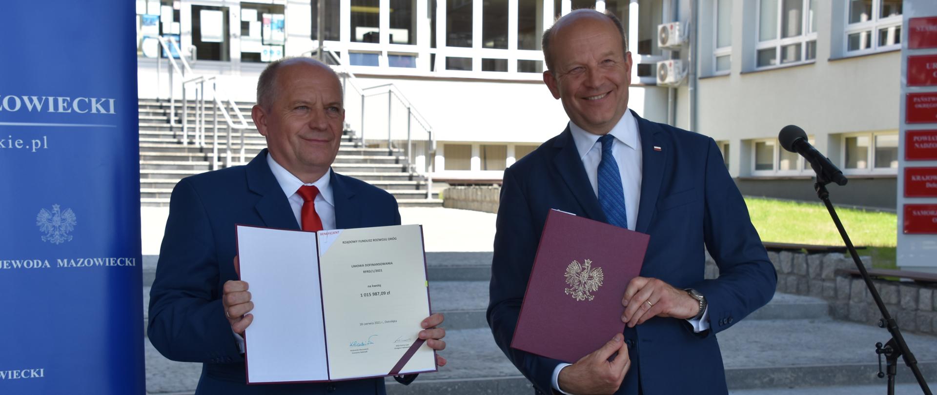 Na zdjęciu znajduje się dwóch mężczyzn pozujących z podpisanymi umowami.