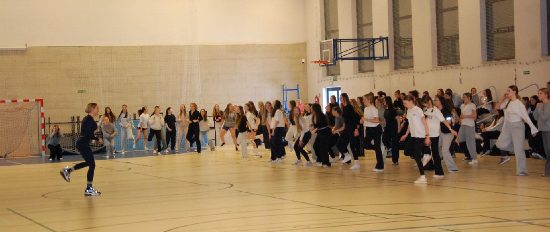 Duża grupa młodzieży ćwiczy z trenerką na sali gimnastycznej