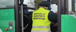 Umundurowany inspektor wielkopolskiej Inspekcji Transportu Drogowego stoi w przednim wejściu kontrolowanego autobusu szkolnego.
