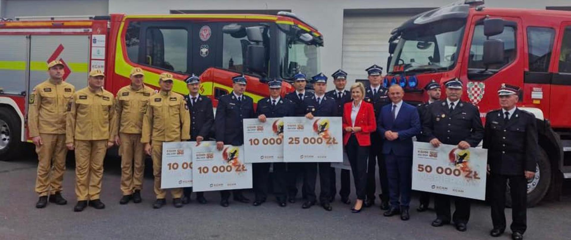 Zdjęcie pamiątkowe uczestników uroczystości na tle dwóch pojazdów pożarniczych