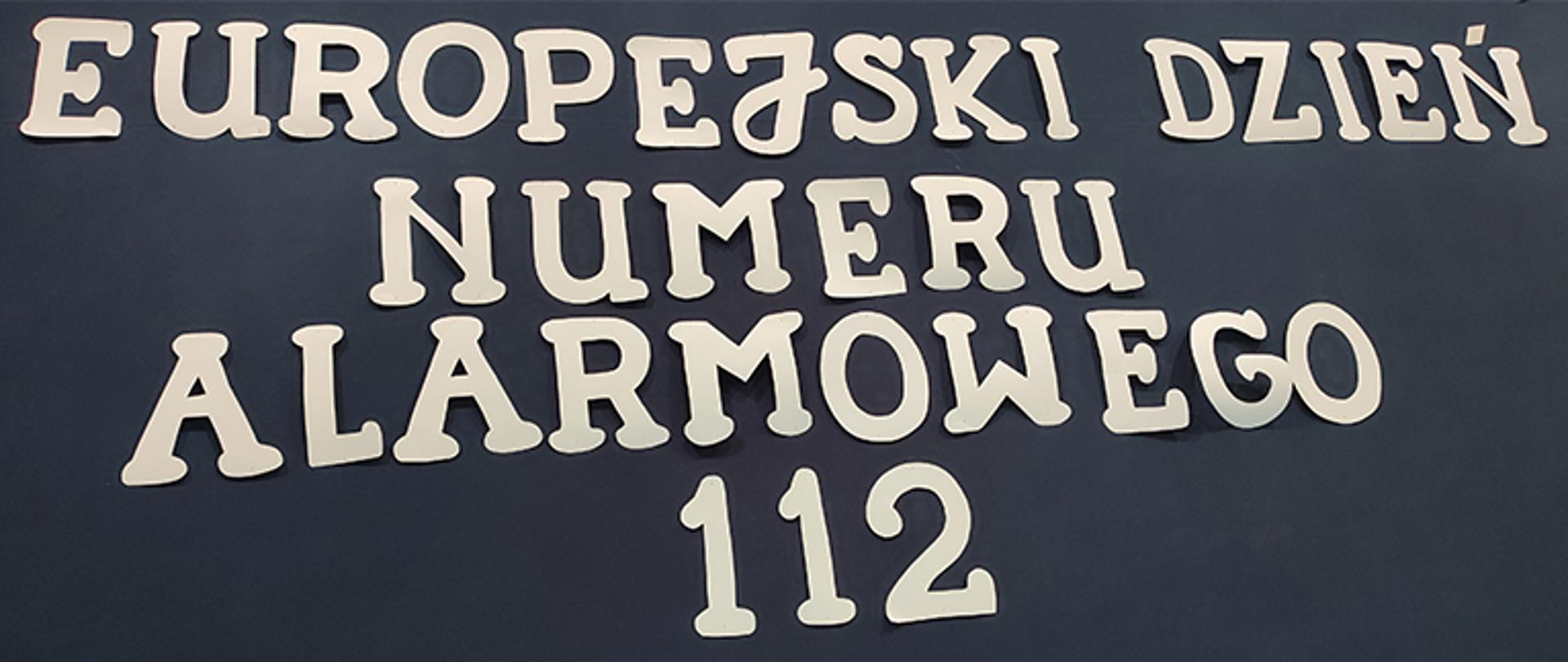 Tablica z ciemnym tłem z literami wyciętymi z papieru barwy białej z napisem Europejski Dzień Numeru Alarmowego 112
