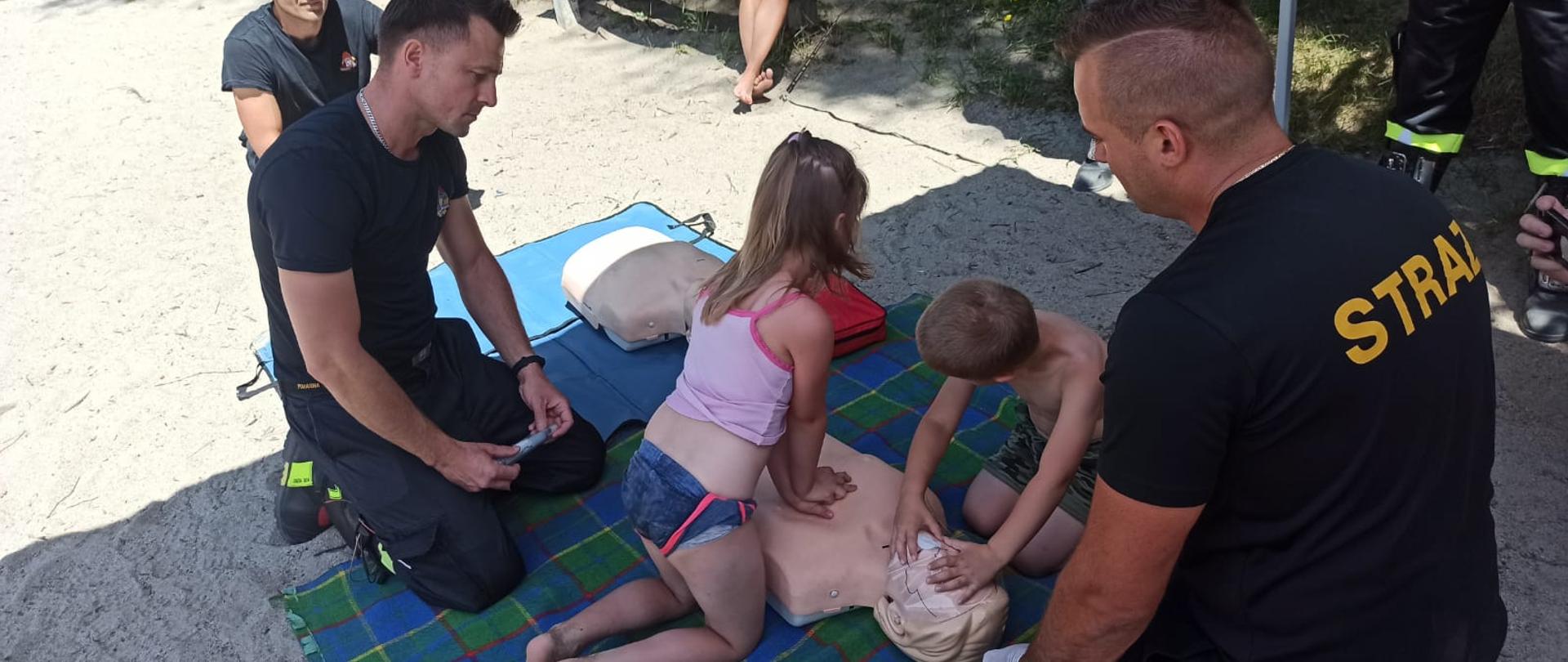 Na zdjęciu strażacy uczą dzieci resuscytacji krążeniowo-oddechowej na fantomie szkoleniowym