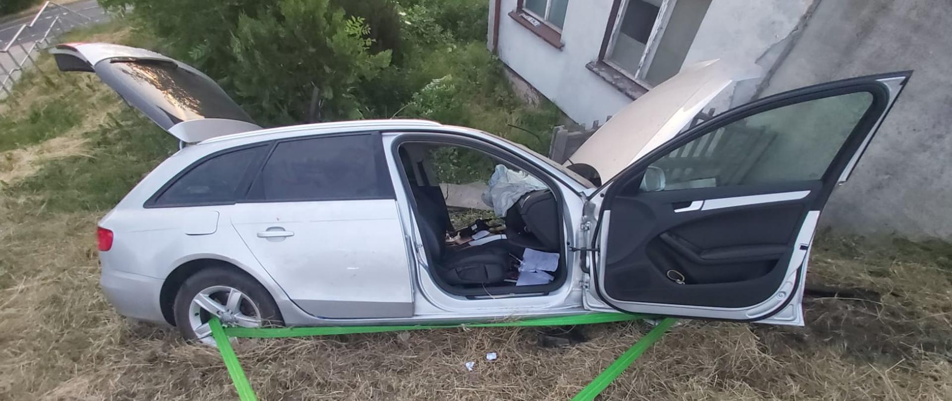 Widać prawy bok pojazdu, drzwi są otwarte, tylna klapa też otwarta, samochód jest blisko budynku