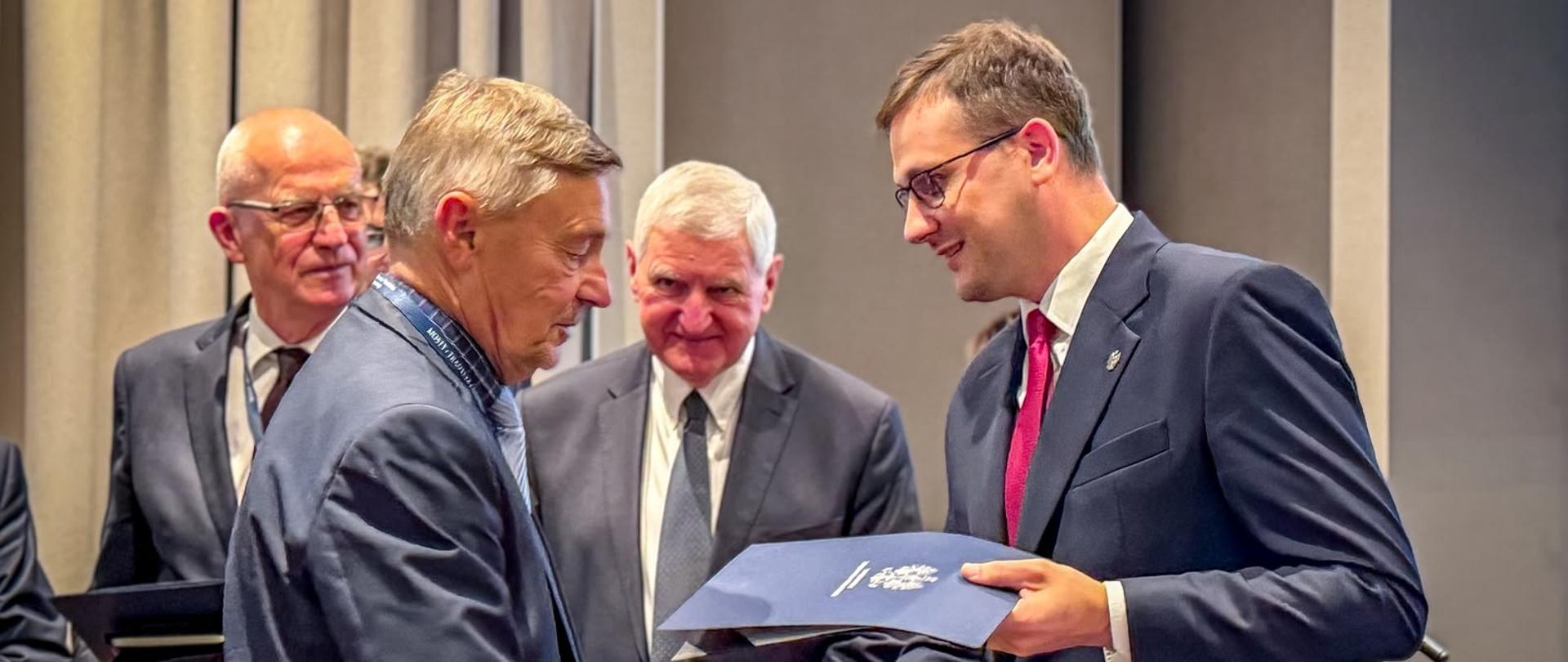 Zdjęcie przedstawia mężczyzn podczas wręczenia wyróżnienia. Z prawej strony Michał Sztybel, Wojewoda Kujawsko – Pomorski. Odbywa się to podczas 35-lecia Związku Mostowców RP, które odbyło się w Bydgoszczy