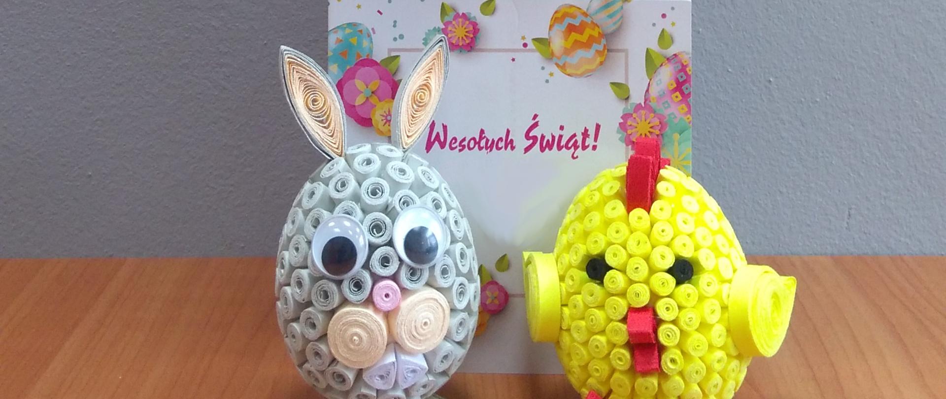 na zdjęciu figurki króliczka i kurczaczka w tle kartka z napisem wesołych świąt