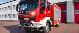 strażacki samochód ciężarowy barwy czerwonej z napisem IVECO stoi przed bramami garażowymi komendy powiatowej Państwowej Straży Pożarnej w Łowiczu, na przodzie pojazdu cztery halogeny zamontowane na srebrnej metalowej rurze, z przody pojazdu znajduje się wyciągarka w czarnym pokrowcu, na lewych przednich drzwiach znajduje się godło PSP, na tylnych widnieją duże białe cyfry z numerem 451E22. Za pojazdem po prawej stronie dwie bramy barażowe barwy czerwonej, po lewej stronie pojazdu widać dwa rzędy okien na dachu budynku dwa maszty antenowe z odciągami. Pogoda słoneczna, niebo prawie bezchmurne