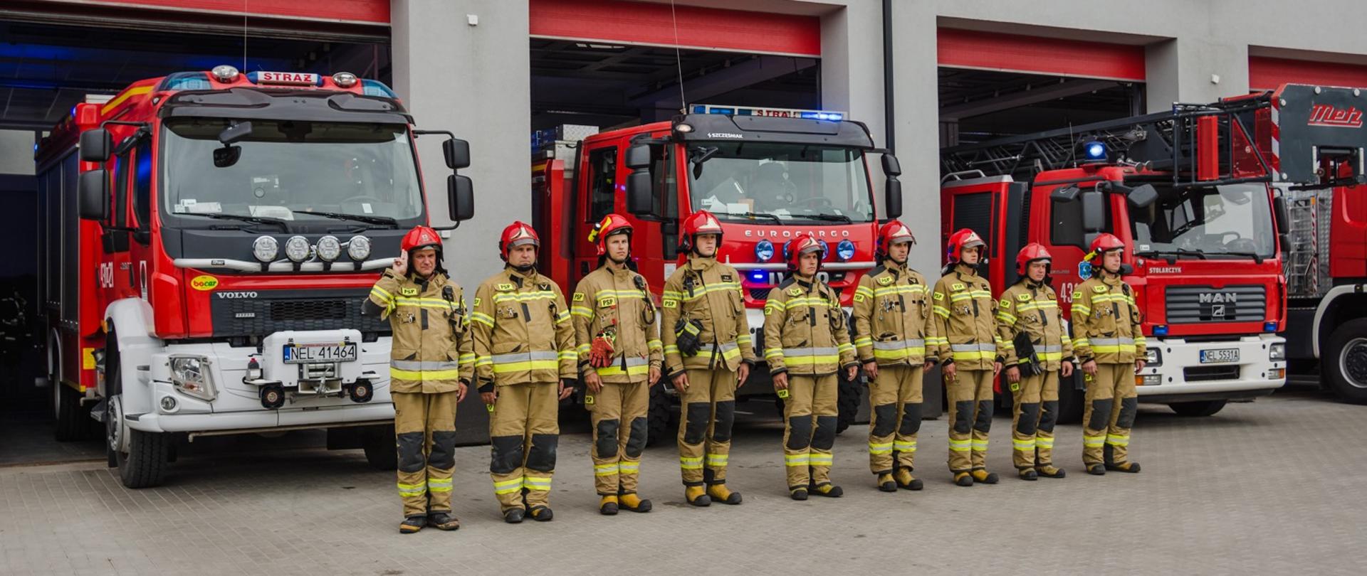 Zdjęcie przedstawia zmianę służbową JRG PSP w Ełku na placu zewnętrznym KP PSP w Ełku, w tle wystawione z garaży samochody pożarnicze.