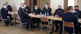 2. Widok z boku. Za stołami na sali OSP siedzą uczestnicy spotkania w mundurach strażackich i maseczkach ochronnych. 