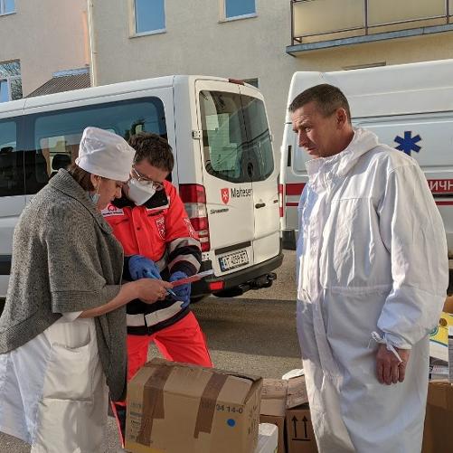 Trzy osoby przed minivanem i między paczkami podpisują dokumenty