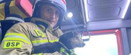 Widok z boku, strażak siedzący w kabinie pojazdu trzyma na rękach uratowanego psa. 