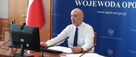 Wojewoda opolski podczas konferencji prasowej prowadzonej online, siedzi przed monitorami.