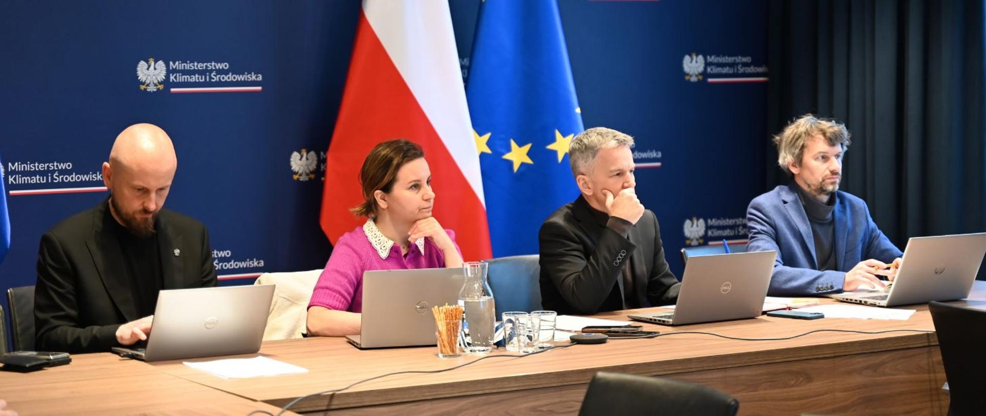 Na zdjęciu widać Pawła Jaworskiego, Urszulę Zielińską, Szymona Tumielewicza oraz Louisa Courseau. Wszyscy siedzą za biurkiem, mają przed sobą otwarte laptopy. Na biurku stoją również szklanki, karafka z wodą oraz paluszki. W tle widać ściankę z logotypem Ministerstwa Klimatu i Środowiska oraz flagę Polski i Unii Europejskiej.
