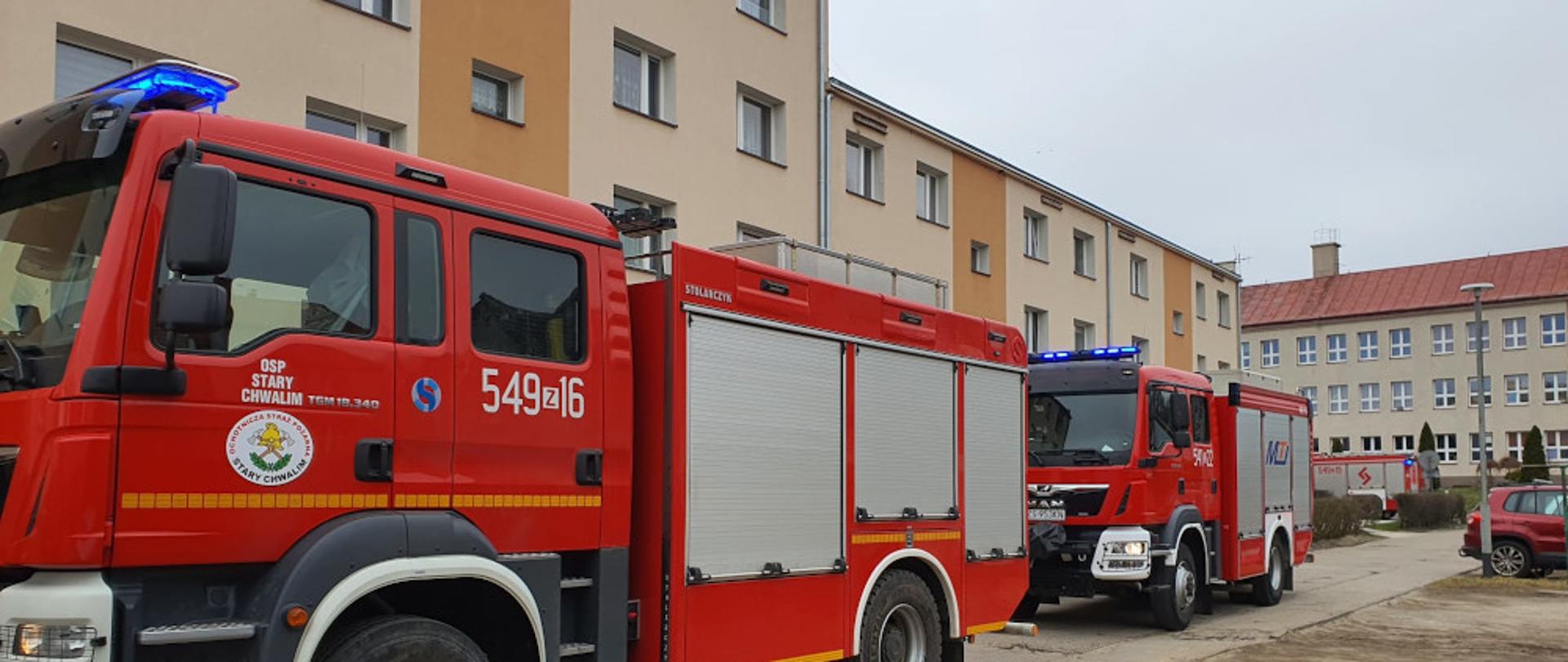 Pożar mieszkania w budynku wielorodzinnym w miejscowości Barwice - dwa samochody ratowniczo-gaśnicze, koloru czerwonego na tle bloku mieszkalnego