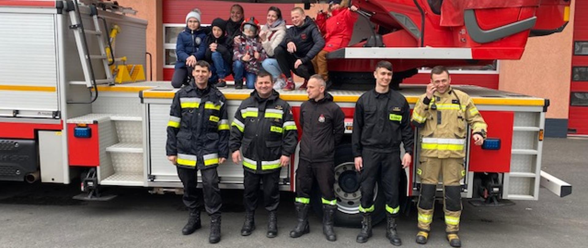 Wizyta Ukraińskich dzieci w JRG - Strażacy i dzieci z opiekunami na tle drabiny pożarniczej i JRG Polkowice