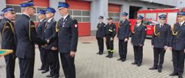 Zdjęcie przedstawia strażaków, którzy stoją na placu przed komendą podczas uroczystości obchodów dnia strażaka. Zastępca Komendanta Wojewódzkiego PSP wręcza awans na wyższy stopień strażakowi. 
