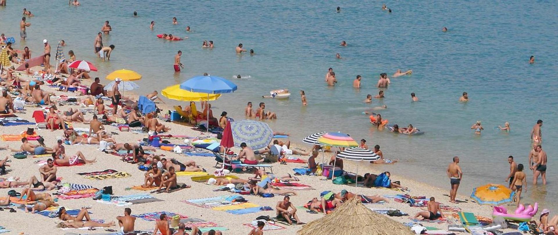 osoby w strojach kąpielowych plażujący i kąpiący się w wodzie