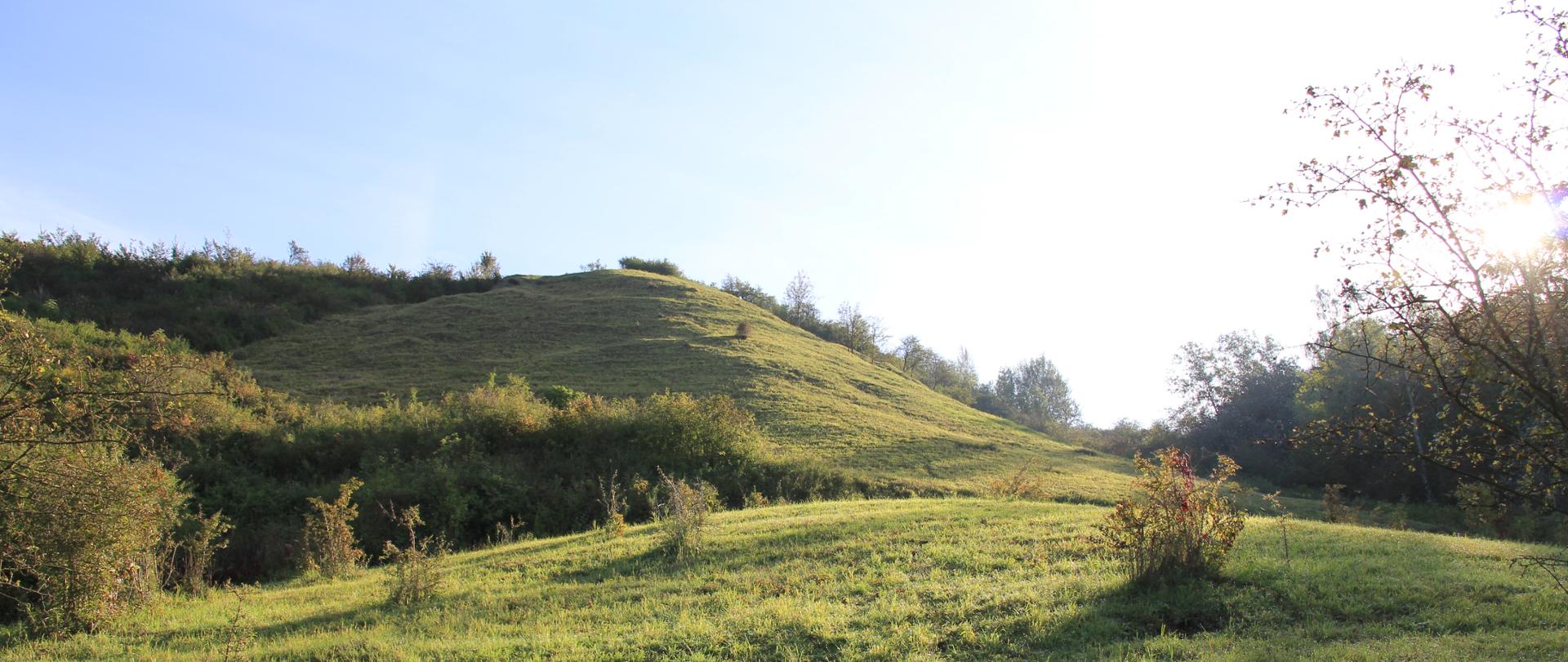 Fragment błękitnego nieba, wzgórze pokryte zieloną trawą.